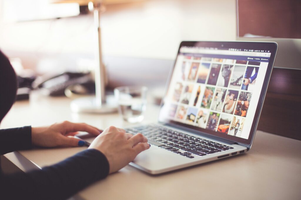 Close-up of hands typing on a laptop with an image gallery open on the screen.